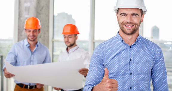 This image shows a man doing a thumbs-up sign. He is wearing a hard hat.