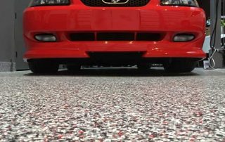 This image shows a flake epoxy floor. A red car is parked there.